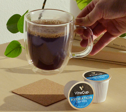 Clear mug with coffee, VitaCup hydration coffee pod, and a hand holding the mug on a wooden surface.