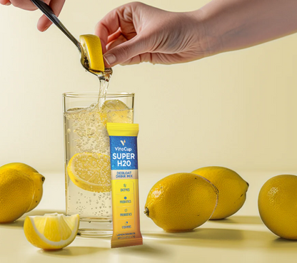 Person adding a Vitacup Super H2O drink mix packet to a glass of water with lemons on a light background